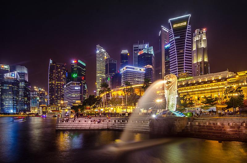 Photo of the Singapore Merlion at night with Fullerton Hotel at the back and other skyscrapers lit up by colourful lights